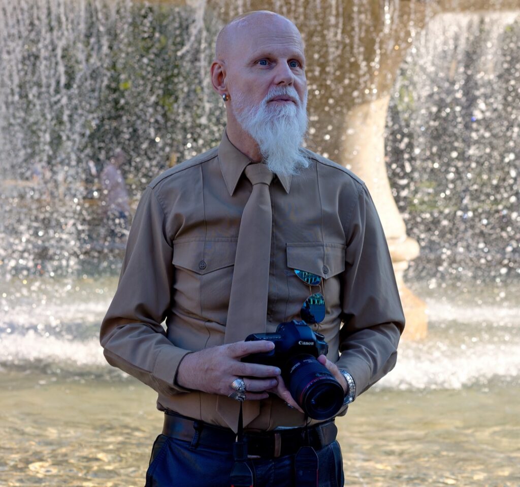 Klaus steht mit einer Canon Kamera vor einem Brunnen an der Konstablerwache in Frankfurt.
